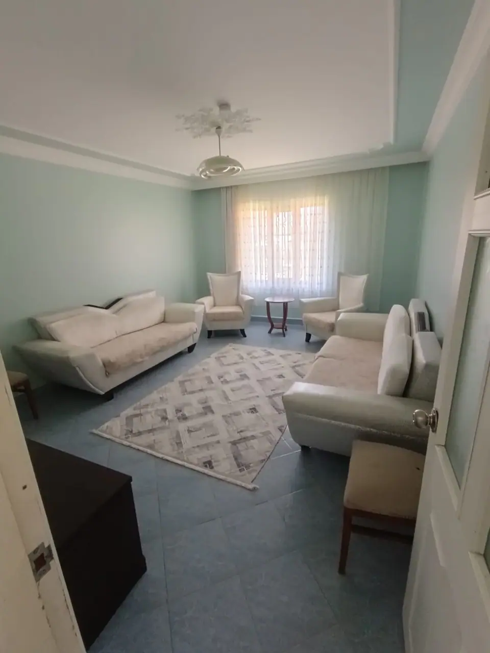 Pencere önünde berjerler, kanepeler ve geometrik desenli halıyla salon