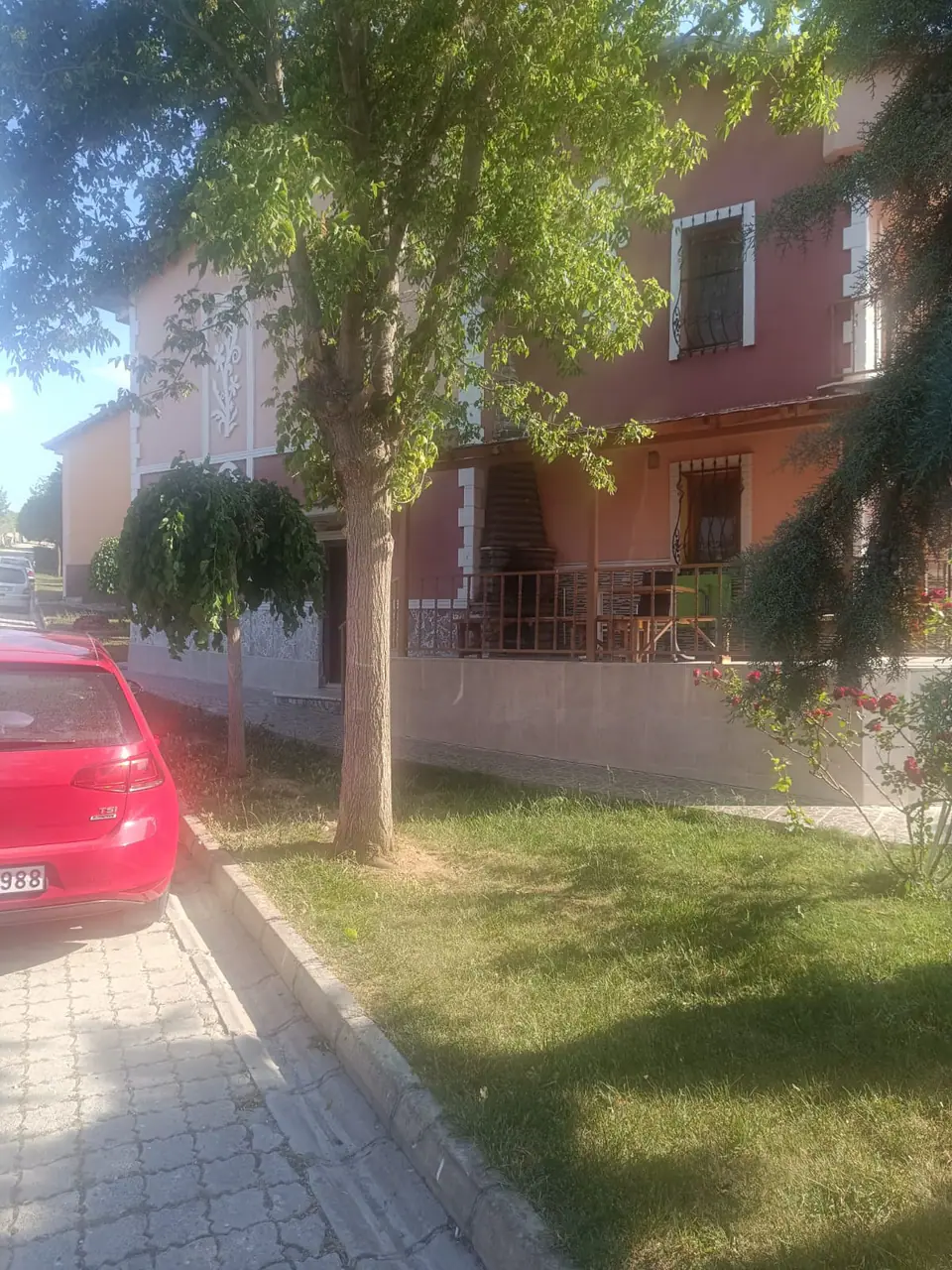 Ağaçlı sokaktan villanın yan cephesi ve önündeki çimenlik
