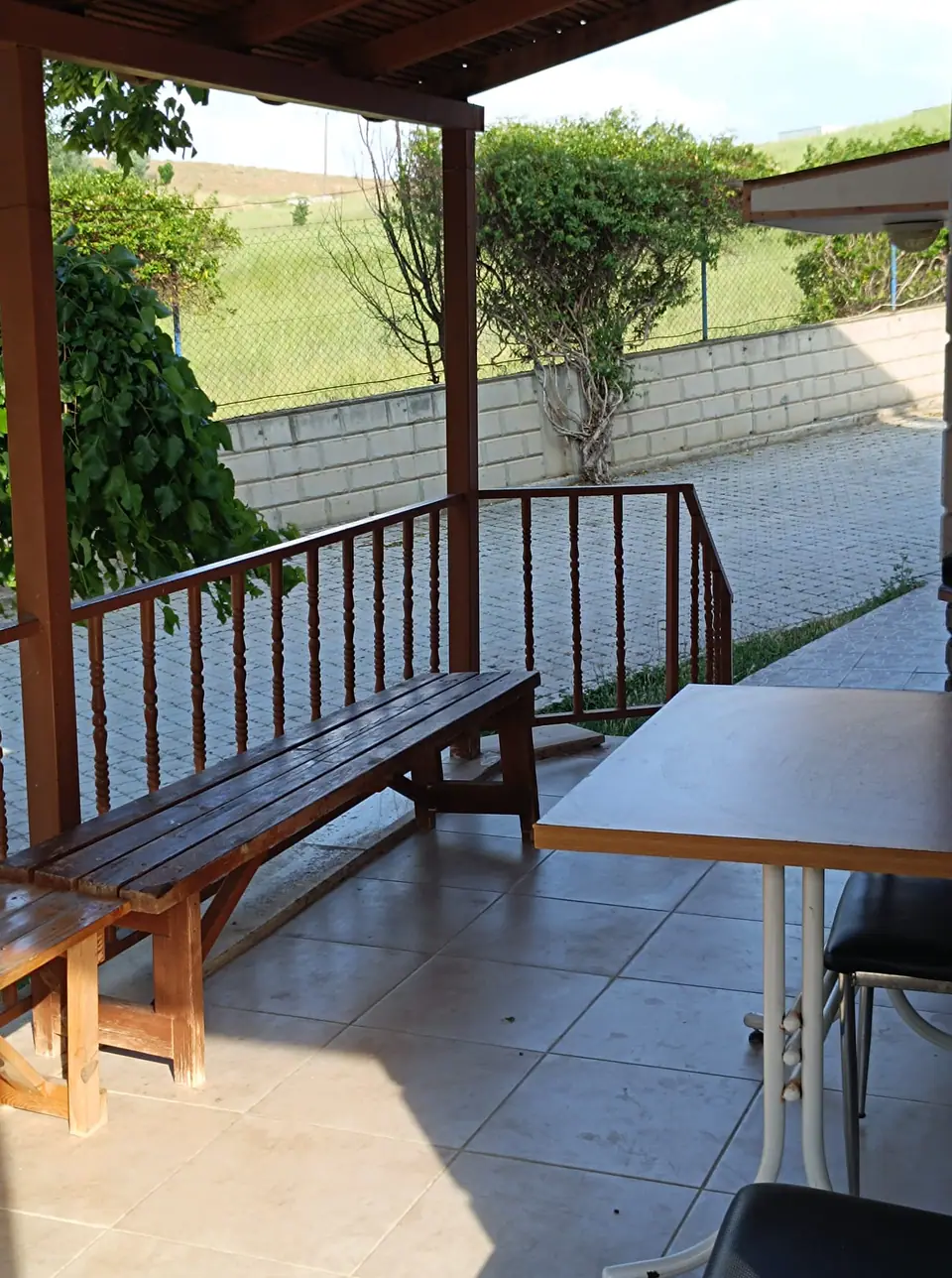 Ahşap banklı, masalı ve yeşil tepeye bakan kapalı teras