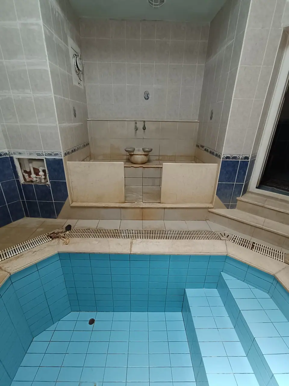 Mavi çinili kapalı termal havuz ve arkasında bakır taslı mermer hamam kurnası