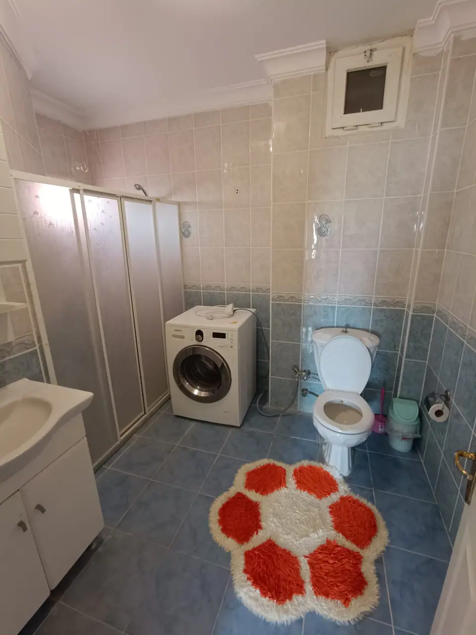 Duş kabinli, çamaşır makineli banyo ve çiçek desenli paspas