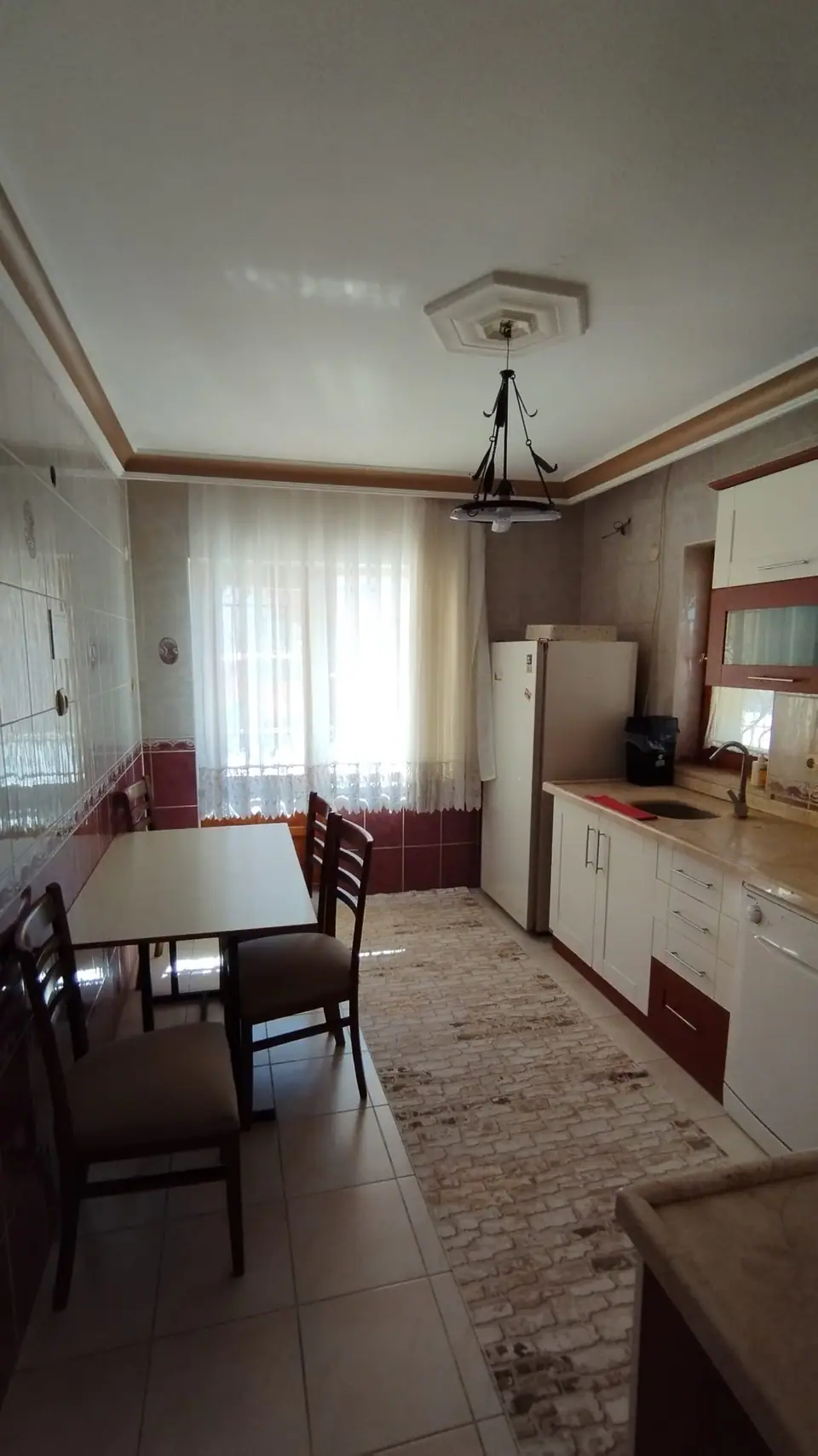 Pencere önünde yemek masası, buzdolabı ve uzun yolluklu mutfak